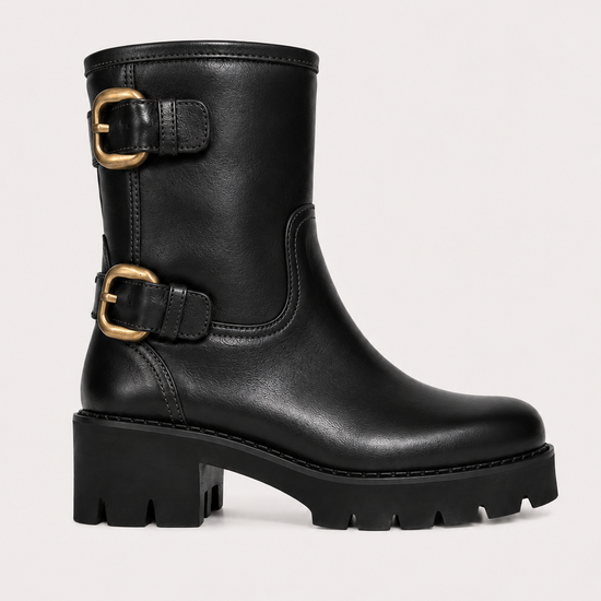 A black leather mid-calf boot with two gold-tone buckle straps and a chunky lug sole, shown against a plain light background.