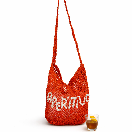 Red woven bag with 'Aperitivo' text next to a glass of juice on a white background
