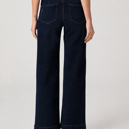 Rear view of a model wearing dark navy wide-leg jeans with decorative stitching on the back pockets, paired with a white top and black sandals, against a light gray studio background.