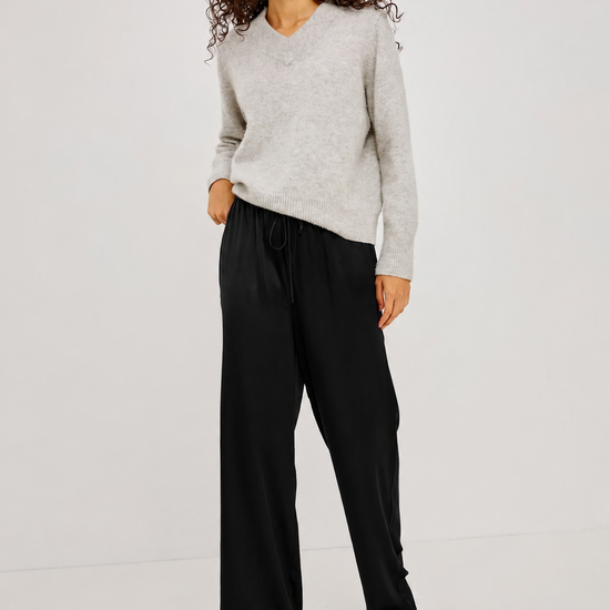 A woman modeling a light gray long-sleeve knit sweater and black wide-leg trousers against a plain light gray studio background.
