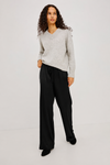 A woman modeling a light gray long-sleeve knit sweater and black wide-leg trousers against a plain light gray studio background.