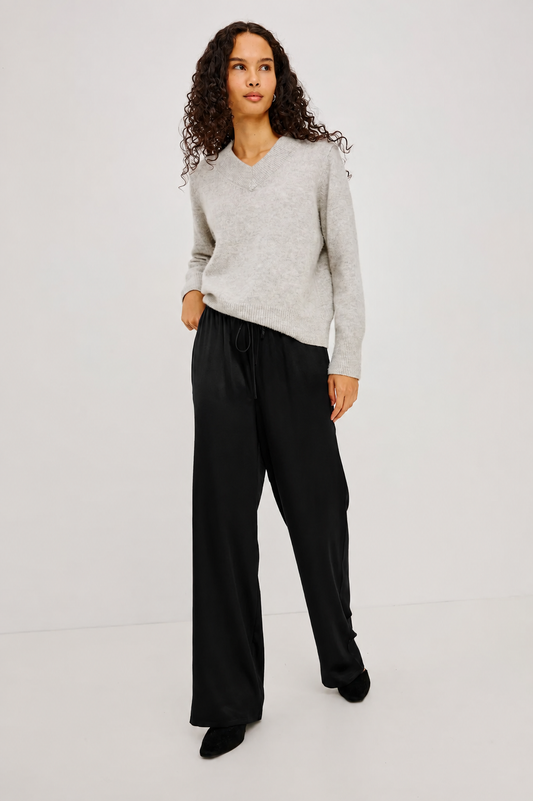 A woman modeling a light gray long-sleeve knit sweater and black wide-leg trousers against a plain light gray studio background.