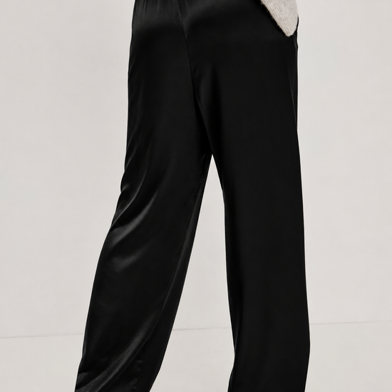 A person wearing black wide-leg satin trousers and a light gray sweater, shown from the back against a plain light gray studio background.