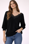 Woman wearing a black sweater with lace neckline and blue jeans on a white background