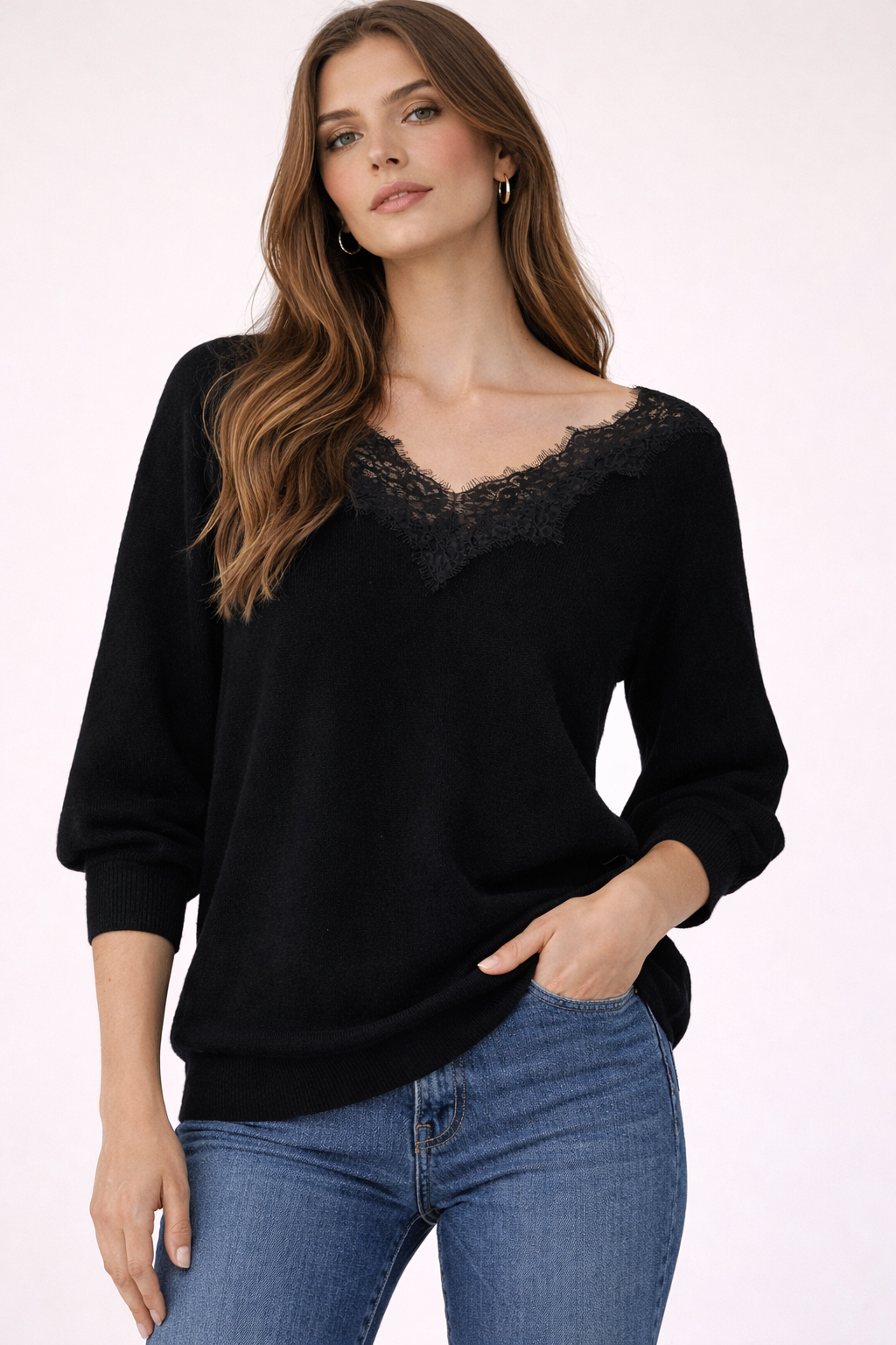 Woman wearing a black sweater with lace neckline and blue jeans on a white background