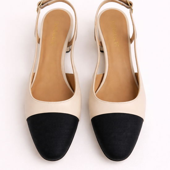 Pair of cream heeled slingback shoes with black toe block on a white background
