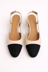 Pair of cream heeled slingback shoes with black toe block on a white background