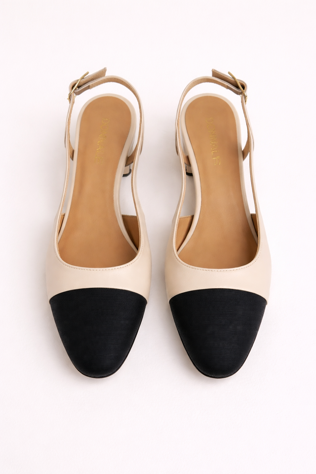 Pair of cream heeled slingback shoes with black toe block on a white background