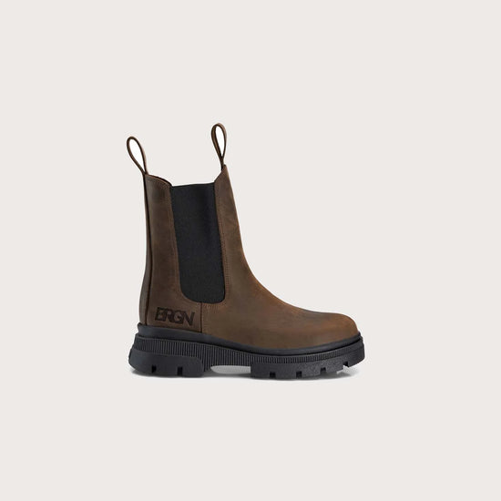 A single brown leather Chelsea-style boot with a black elastic side panel and a black lug sole, shown on a plain light beige background. The brand name is visible on the side of the sole.