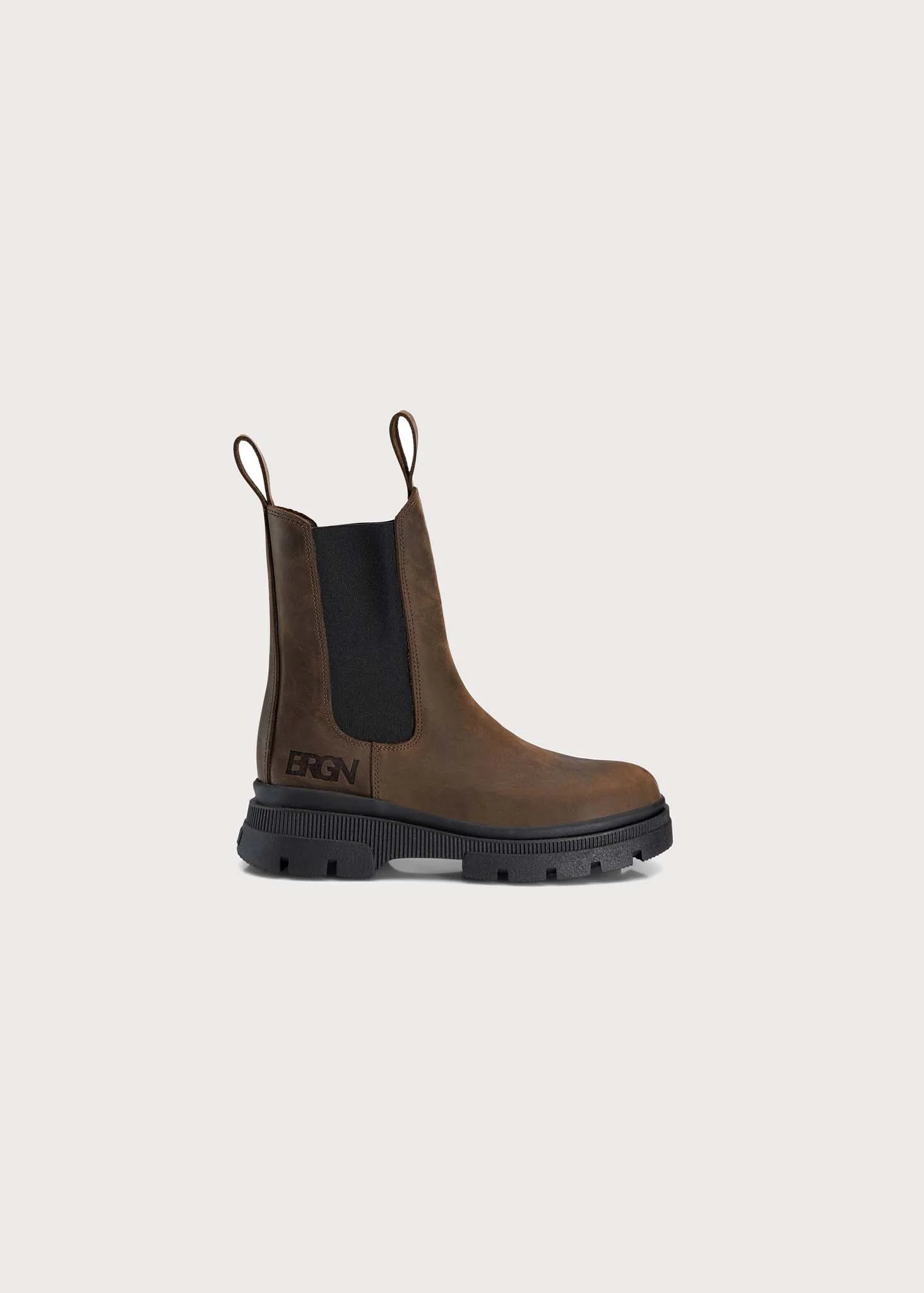 A single brown leather Chelsea-style boot with a black elastic side panel and a black lug sole, shown on a plain light beige background. The brand name is visible on the side of the sole.