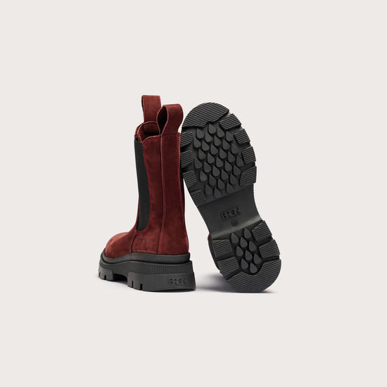 A pair of red suede Chelsea-style boots with black elastic side panels and black lug soles, shown from the back on a light gray background.