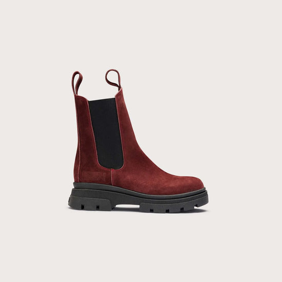 A single dark red suede Chelsea boot with a black elastic side panel and a chunky black lug sole, shown in profile against a light beige background.