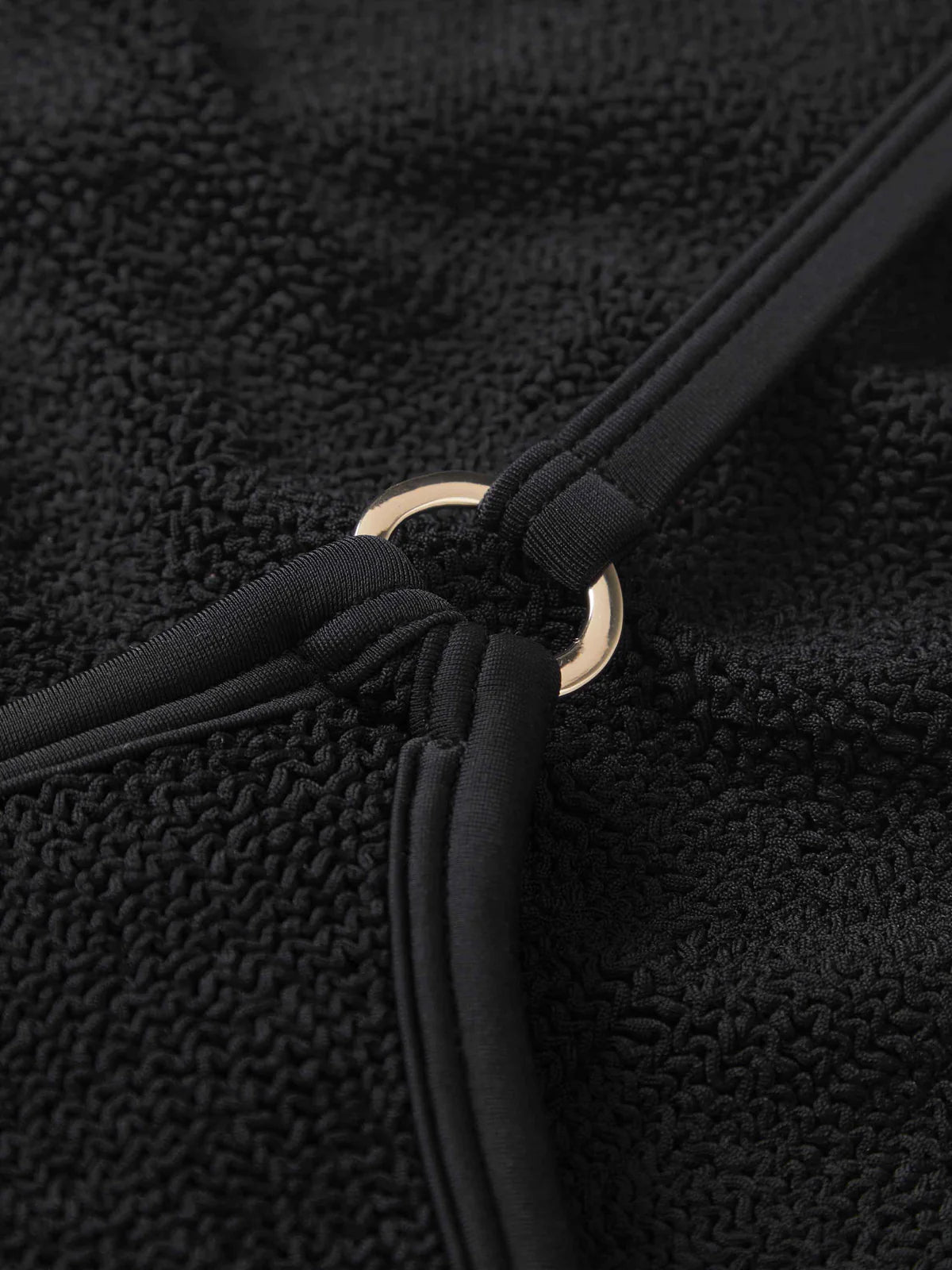 Close-up of a black textured fabric with a gold ring detail.