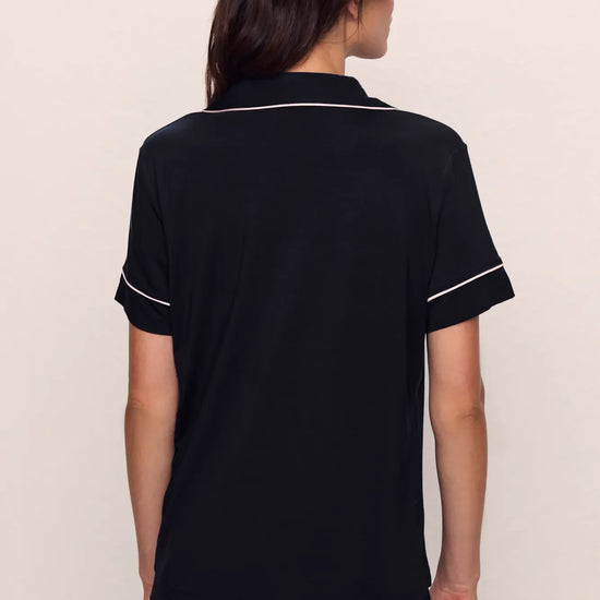 Person wearing a black pajama set with white piping from Eberjey