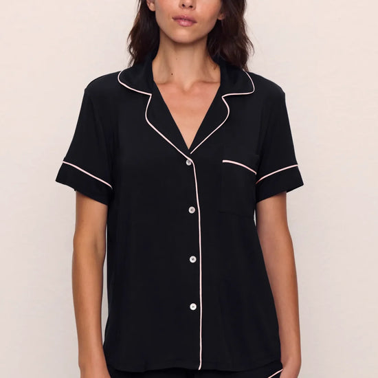 Woman wearing a black pajama set with white piping from Eberjey