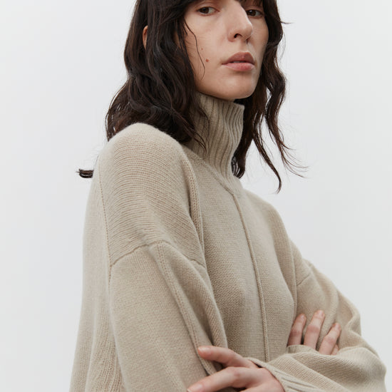 Beige wool dress with a funnel neck and long sleeves close up of drop shoulder