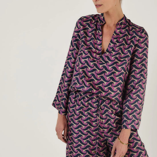 Woman wearing a purple and pink patterned outfit including trousers from Mondo Corsini on a white background