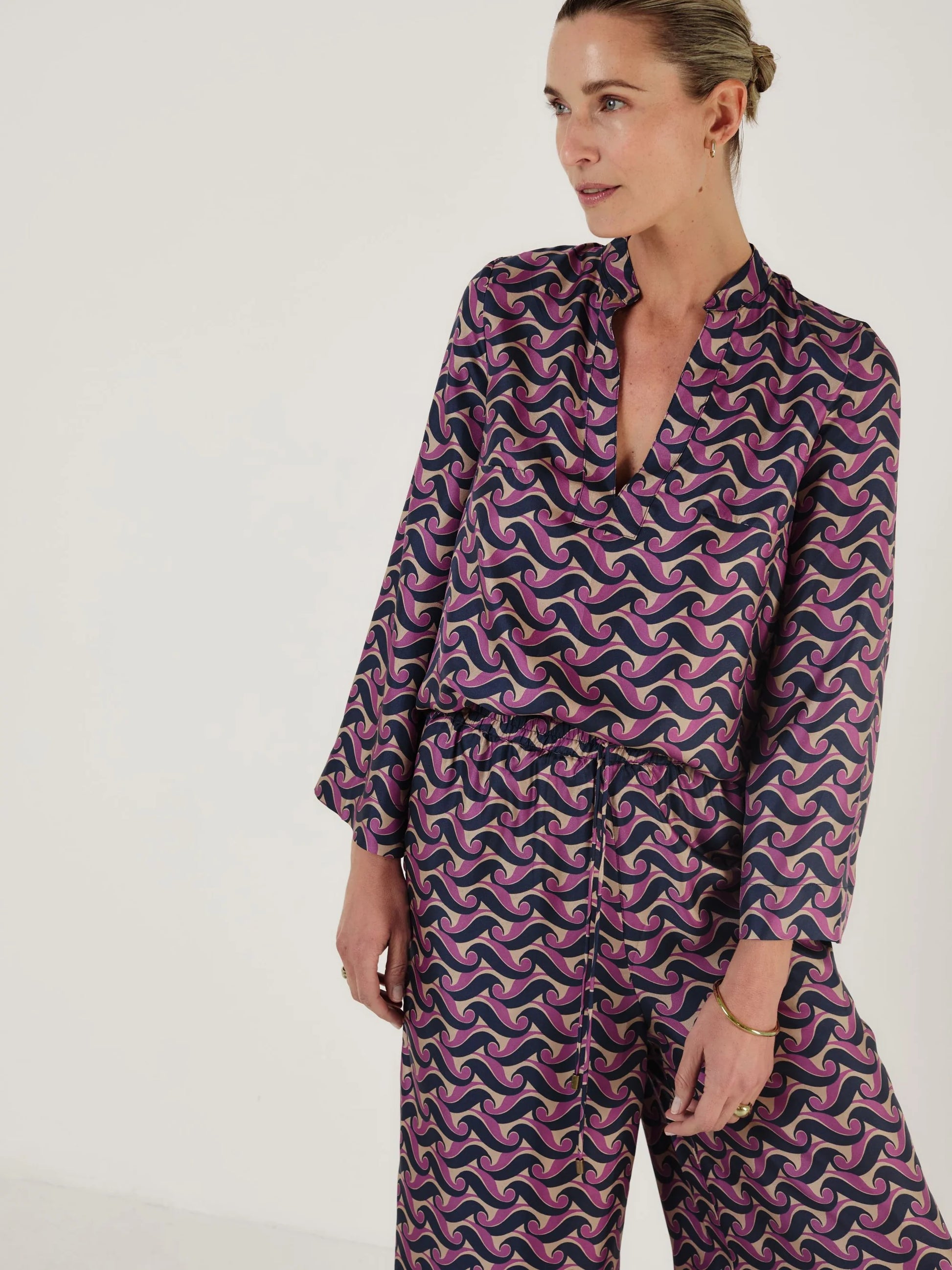 Woman wearing a purple and pink patterned outfit including trousers from Mondo Corsini on a white background