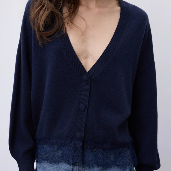 A woman wearing a navy blue knit cardigan with a deep V-neck, button-front closure, and a textured hem, paired with light blue denim.