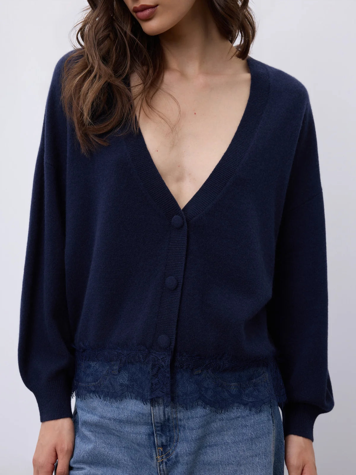 A woman wearing a navy blue knit cardigan with a deep V-neck, button-front closure, and a textured hem, paired with light blue denim.