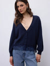 A woman wearing a dark navy blue knit cardigan with a deep V-neck and button-front closure, paired with light blue jeans, photographed against a plain light gray studio background.