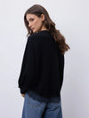 A woman wearing a black knit sweater and blue jeans, photographed from the back against a plain light gray studio background.