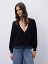 A woman wearing a black long-sleeve cardigan with a deep V-neck and button front, paired with light blue jeans, against a plain light gray studio background.