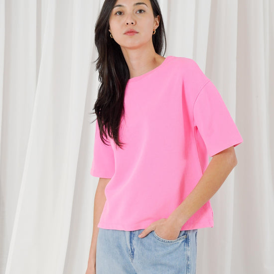 Person wearing a bright pink oversized t-shirt and light blue jeans against a white curtain background