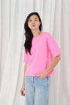 Person wearing a bright pink oversized t-shirt and light blue jeans against a white curtain background