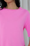 A close-up of a person wearing a bright pink short-sleeve crewneck top, showing the neck, collar, and shoulder area against a light neutral background.