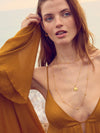 Woman wearing a mustard yellow dress with gold jewelry on a blurred natural background