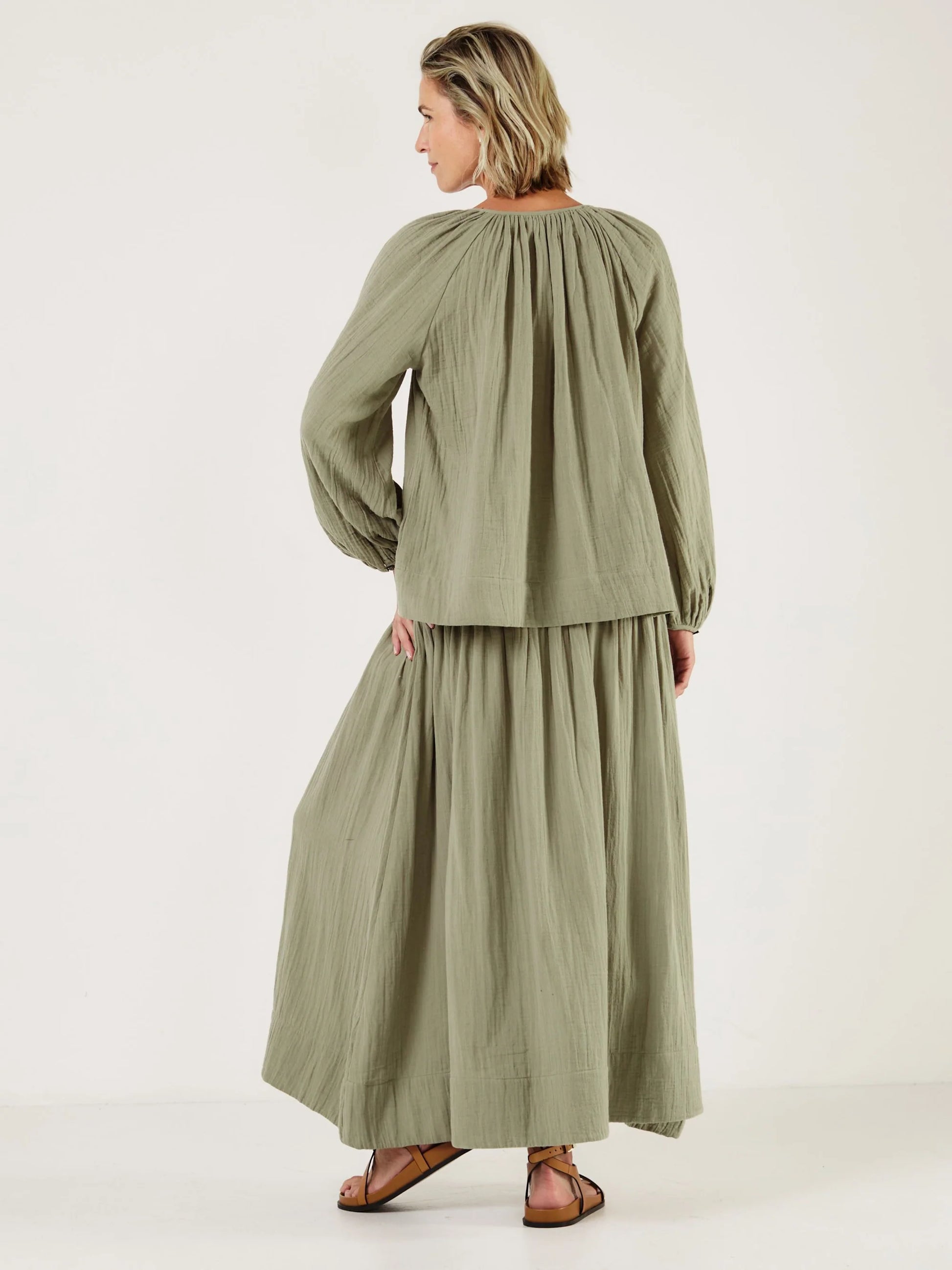 Woman wearing a green outfit, including shirt from Mondo Corsini, on a white background. Rear View