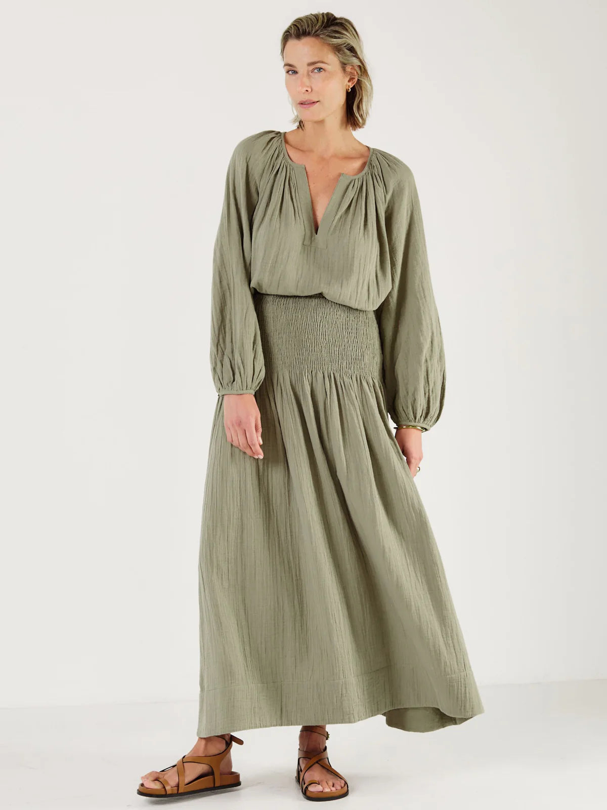 Woman wearing a green outfit, including shirt from Mondo Corsini, on a white background. Tucked in.