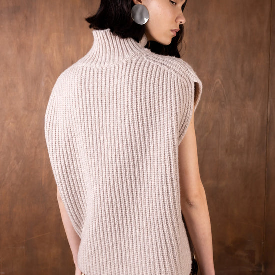 Woman wearing a beige knitted vest against a brown background