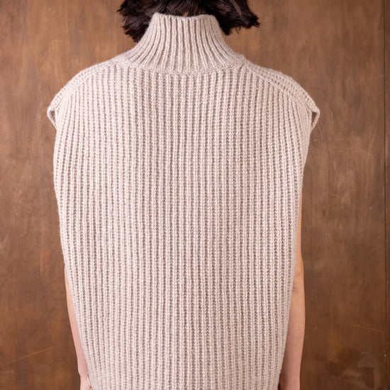 Person wearing a beige knitted vest against a brown background