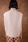 Person wearing a beige knitted vest against a brown background