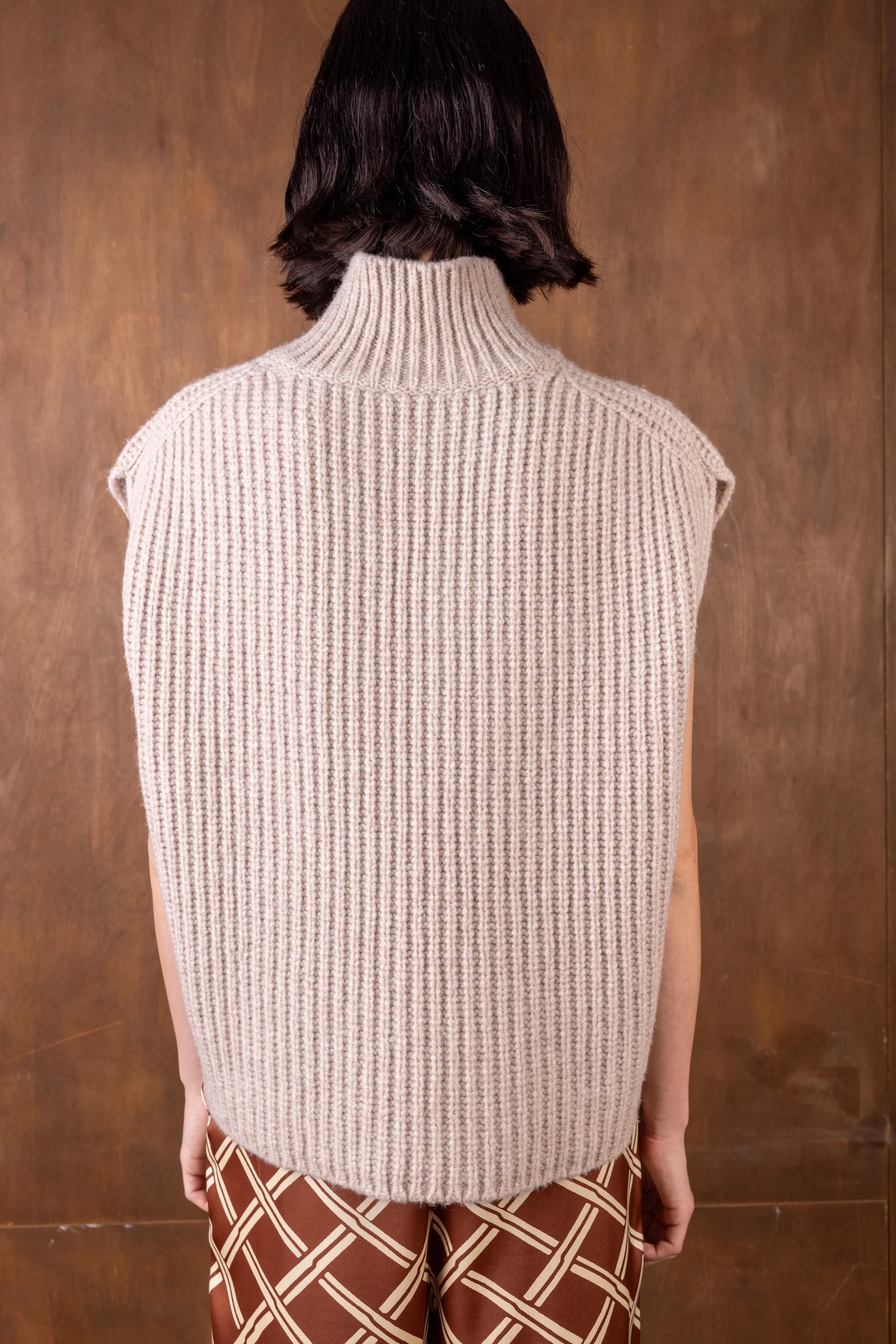 Person wearing a beige knitted vest against a brown background