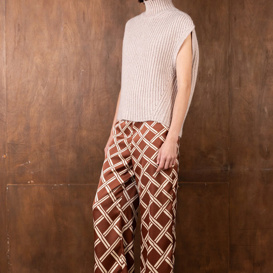 Woman wearing a beige ribbed turtleneck and brown patterned pants against a wooden background