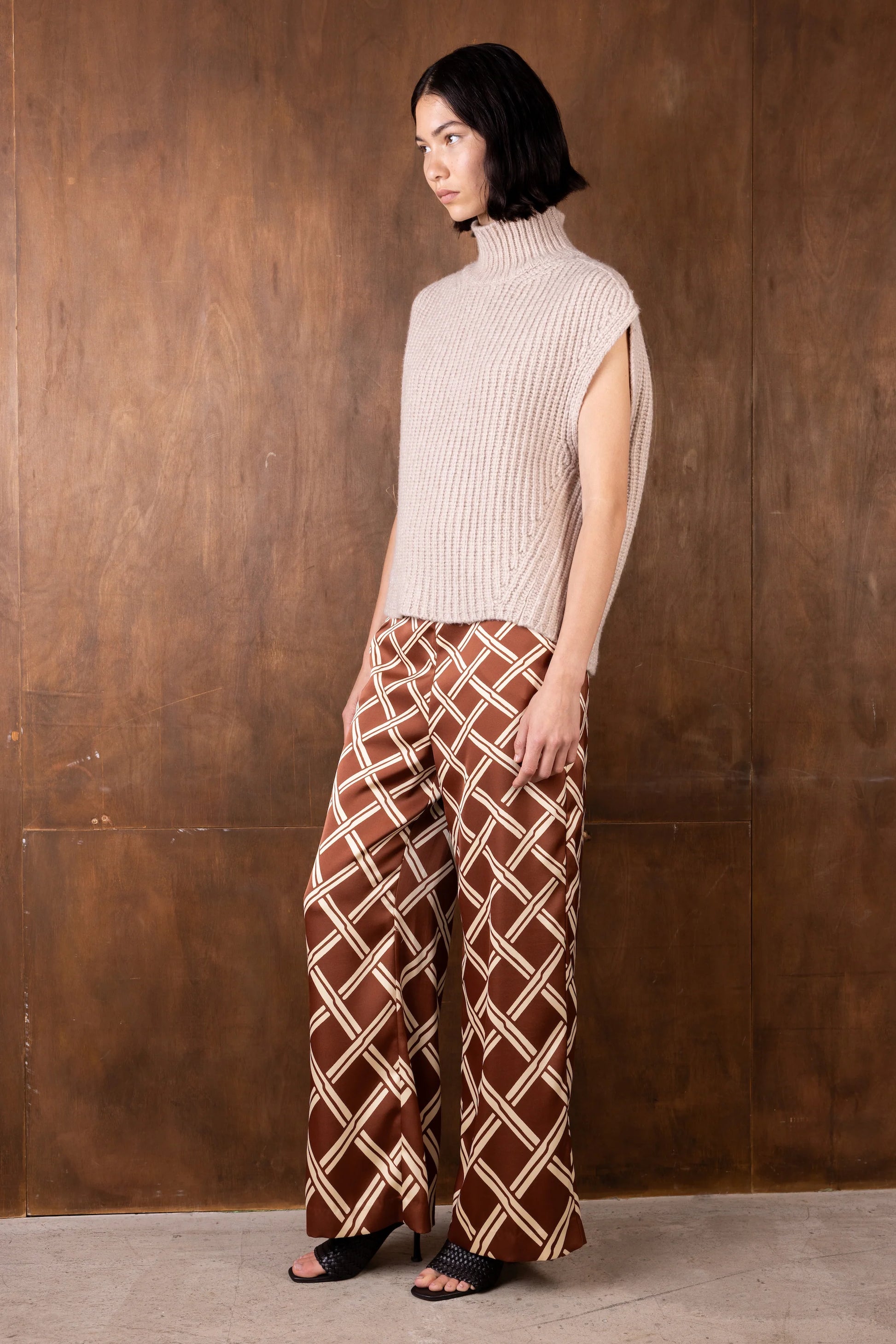 Woman wearing a beige ribbed turtleneck and brown patterned pants against a wooden background
