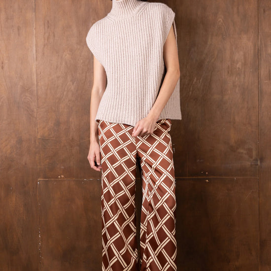 Woman wearing a sleeveless ribbed knit top and patterned pants against a wooden wall.
