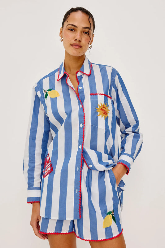 Woman wearing a blue and white striped shirt and shorts with decorative elements on a plain background