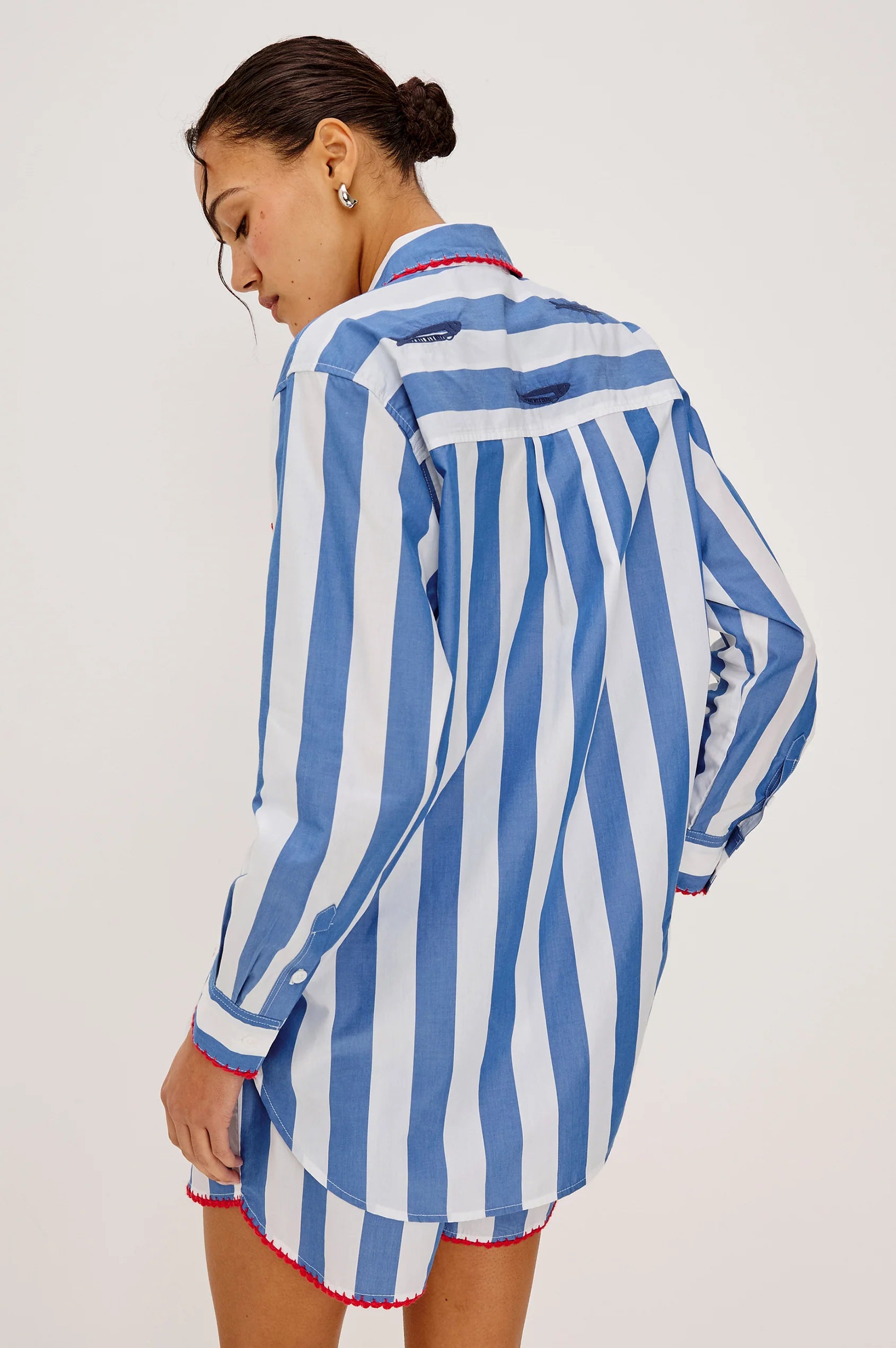 Rear view of Woman wearing a blue and white striped shirt and shorts on a plain background