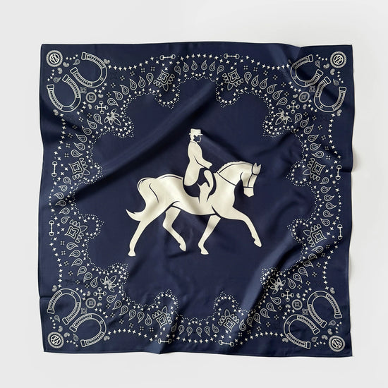 A square navy blue scarf featuring a white equestrian design in the center and an ornate border of horseshoes, dots, and decorative motifs, laid flat on a light gray background.