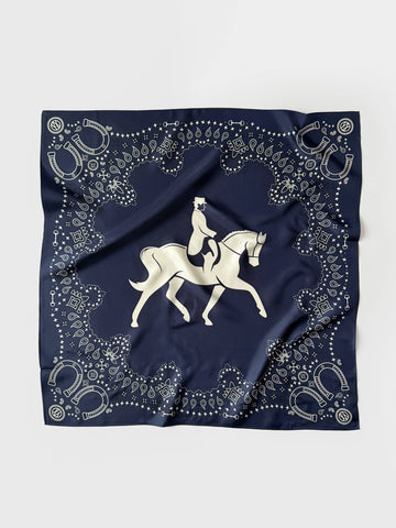 A square navy blue scarf featuring a white equestrian design in the center and an ornate border of horseshoes, dots, and decorative motifs, laid flat on a light gray background.