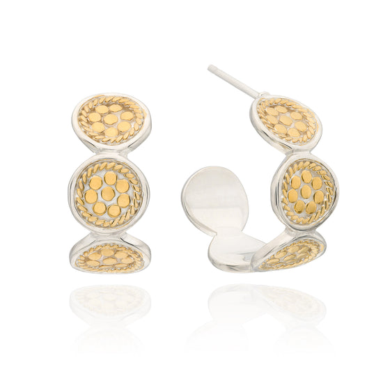 A pair of gold and silver hoop earrings with circular textured details, shown on a clean white background with a soft reflection.