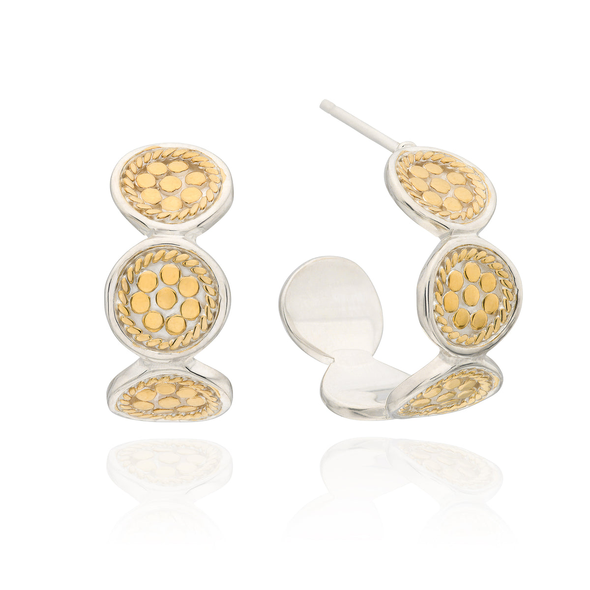 A pair of gold and silver hoop earrings with circular textured details, shown on a clean white background with a soft reflection.