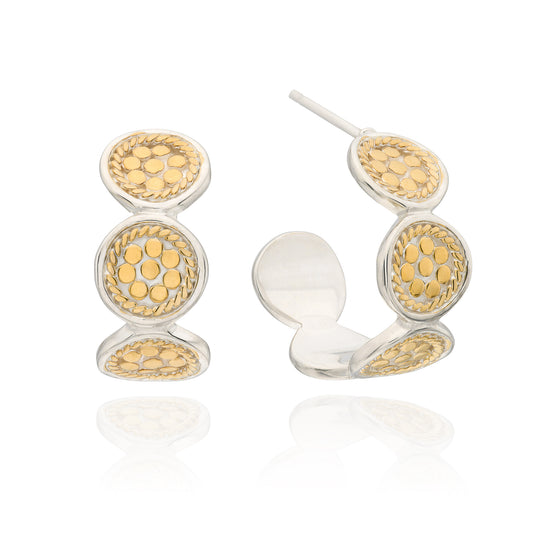 A pair of gold and silver hoop earrings with circular textured details, shown on a clean white background with a soft reflection.