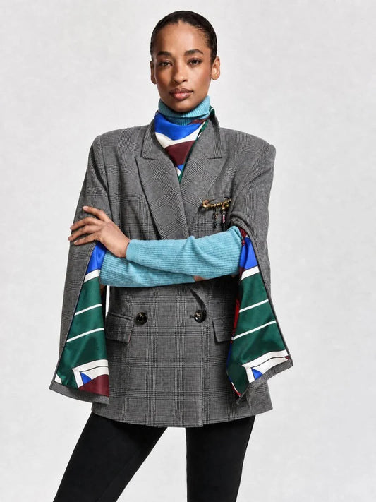 A model wearing a gray double-breasted blazer with a colorful striped scarf draped over the sleeves, styled over a light blue turtleneck sweater and black pants, against a light gray studio background.
