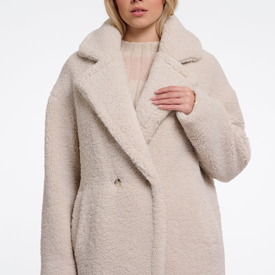 Woman wearing a beige teddy coat on a white background
