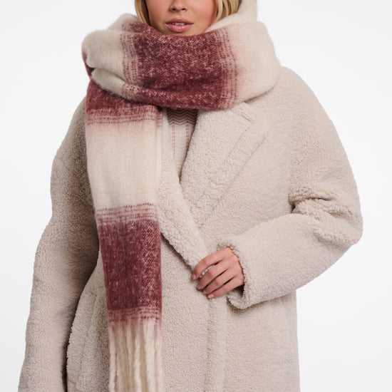 Woman wearing a beige coat and plaid scarf on a white background